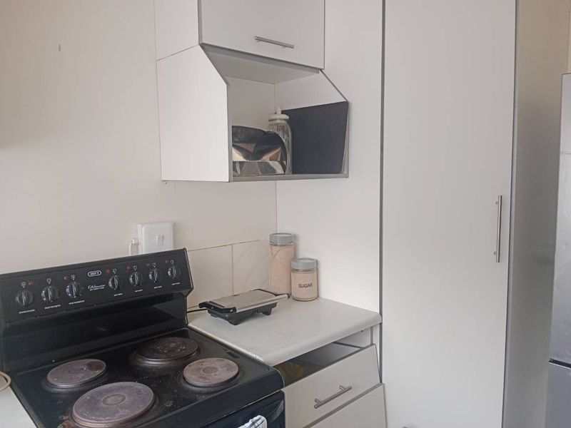 A compact kitchen featuring white cabinetry, a tiled splashback, and a freestanding electric stove with a tall pantry cupboard for storage.