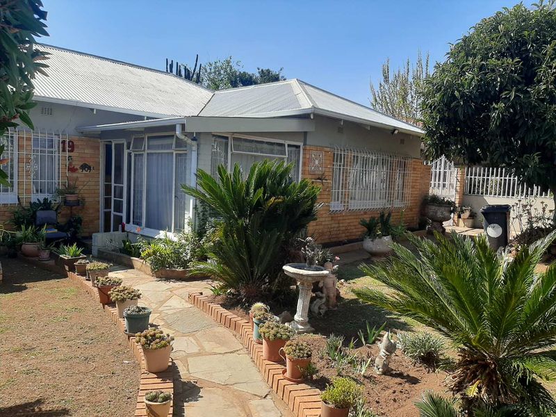 Front view of a single-story brick house featuring a corrugated metal roof, security-barred windows, and a stone-paved garden path.