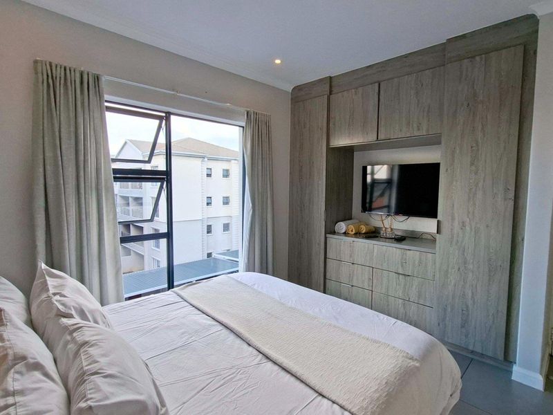 A well-maintained bedroom featuring modern built-in cupboards with integrated storage and a large window providing natural light and an urban view.