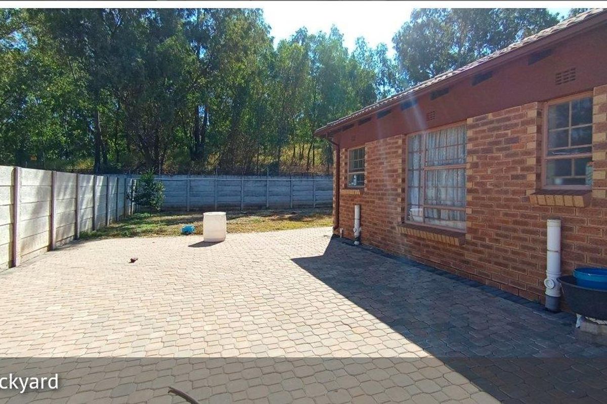 A rear exterior view featuring a paved patio area, brick facade, and a secure precast concrete boundary wall.