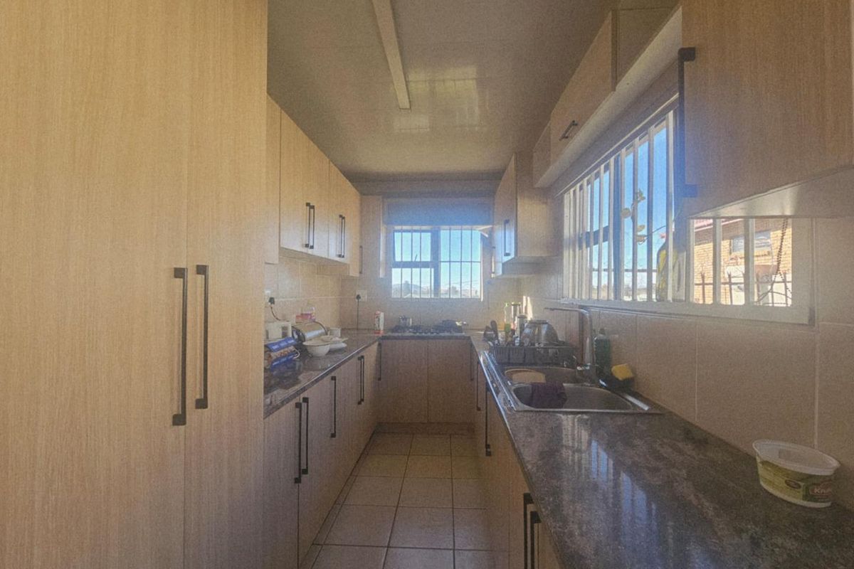A galley-style kitchen featuring light wood-finish cabinetry, granite countertops, a stainless steel sink, and a built-in gas hob.
