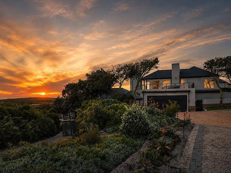 Stunning front elevation of a modern residence at sunset, featuring a paved driveway, double garage, and an elevated balcony with scenic views.