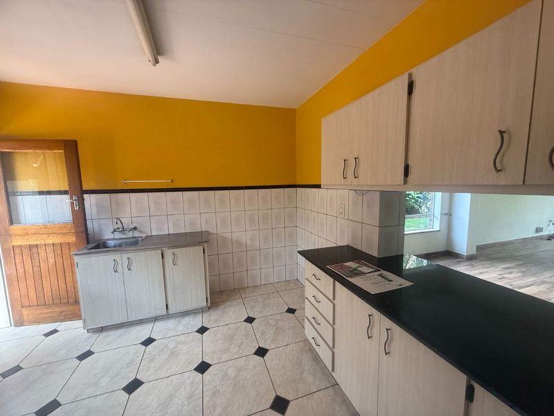 A functional kitchen featuring built-in cabinetry, black granite countertops, a stainless steel sink, and tiled flooring with a decorative pattern.