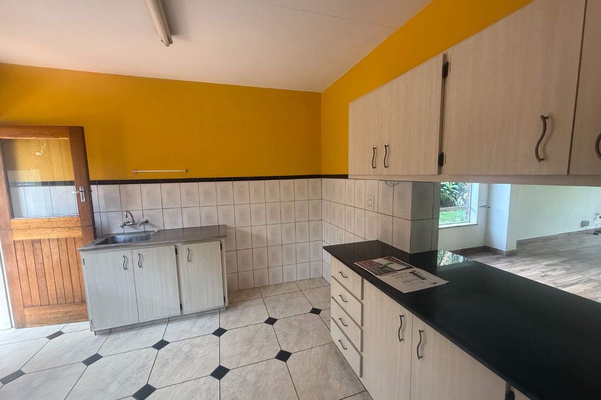 A functional kitchen featuring built-in cabinetry, black granite countertops, a stainless steel sink, and tiled flooring with a decorative pattern.