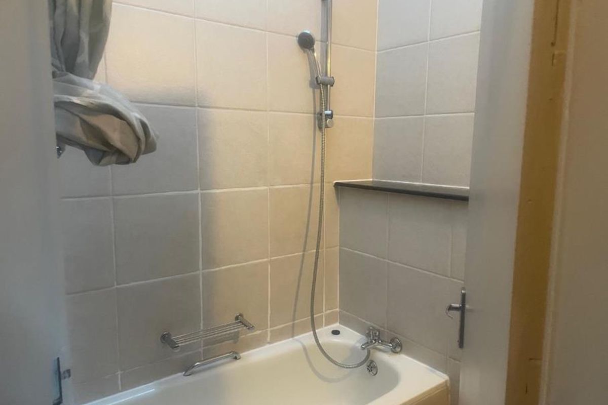 A functional bathroom featuring a bathtub with a handheld shower attachment and tiled wall surrounds.