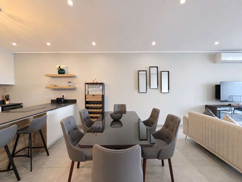 Modern open-plan living and dining area featuring a sleek kitchen island, recessed lighting, and neutral tiled flooring throughout.