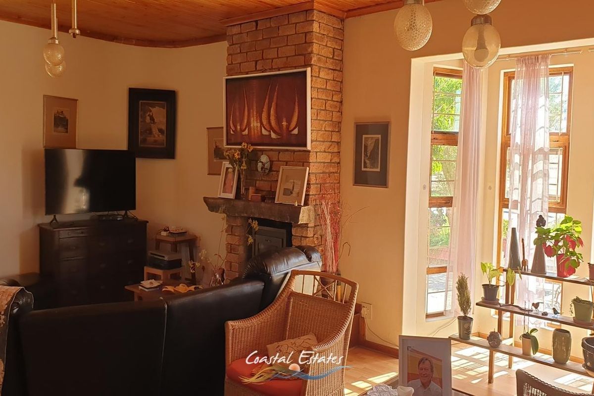 A cozy living room featuring a prominent exposed brick fireplace with a wood-burning stove and a large bay window providing natural light.