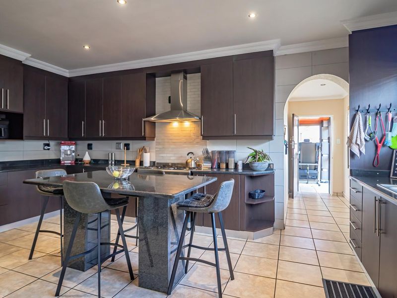 Modern kitchen featuring dark wood cabinetry, granite countertops, a central island, and stainless steel appliances, with tiled flooring and an arched entryway.