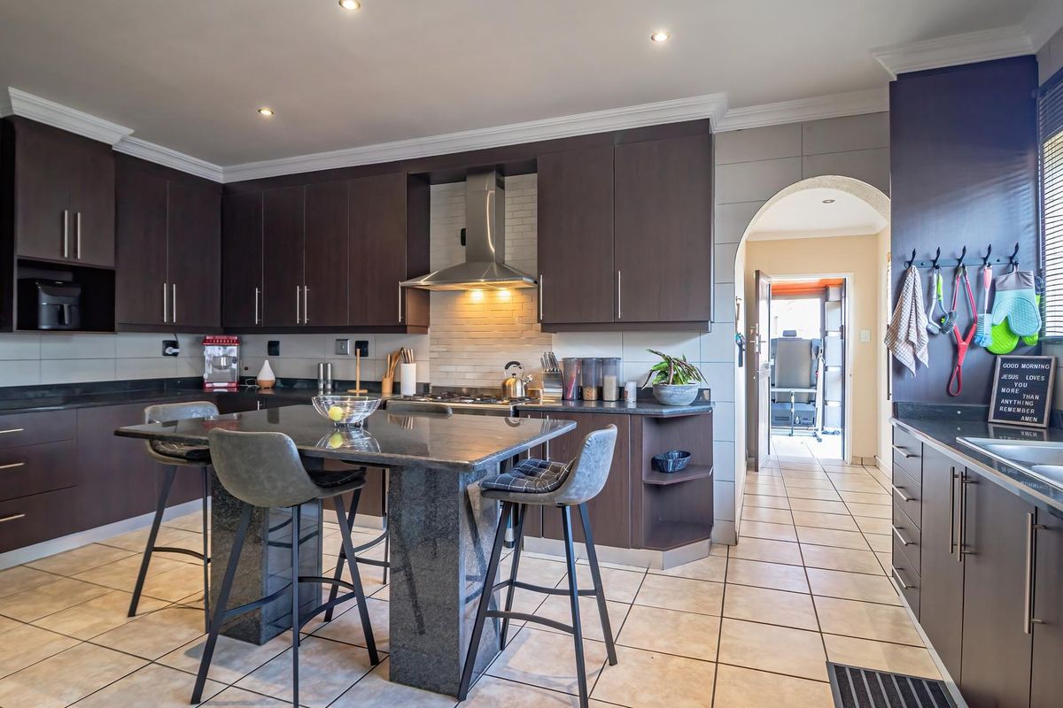 Modern kitchen featuring dark wood cabinetry, granite countertops, a central island, and stainless steel appliances, with tiled flooring and an arched entryway.