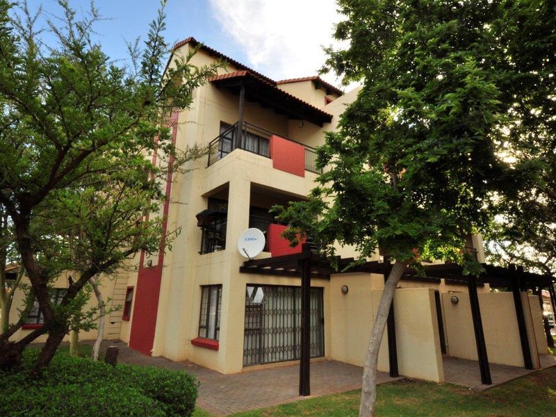Exterior view of a multi-story apartment building featuring private balconies, a ground-floor paved patio with a pergola, and established garden surroundings.