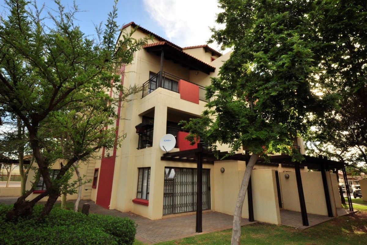 Exterior view of a multi-story apartment building featuring private balconies, a ground-floor paved patio with a pergola, and established garden surroundings.