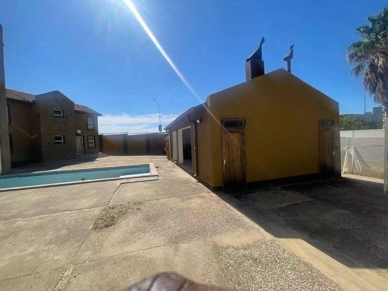 Rear exterior view featuring a swimming pool, paved patio area, and a detached outbuilding with external access doors.
