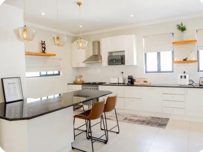 Modern kitchen featuring white cabinetry, dark stone countertops, integrated appliances, and stylish pendant lighting over a breakfast bar island.