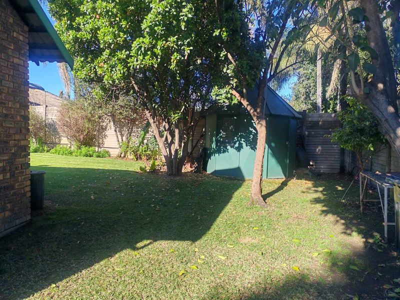 A private backyard garden featuring a lawn, mature trees, perimeter fencing, and a small storage shed.