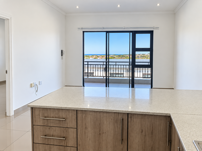 Modern open-plan kitchen area featuring stone countertops, wood-finish cabinetry, and direct access to a balcony with scenic coastal views.