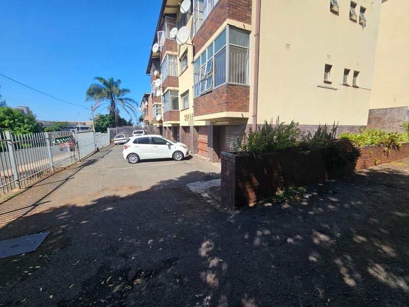 Exterior view of the apartment building facade featuring brick construction, an asphalt driveway, and perimeter metal fencing.