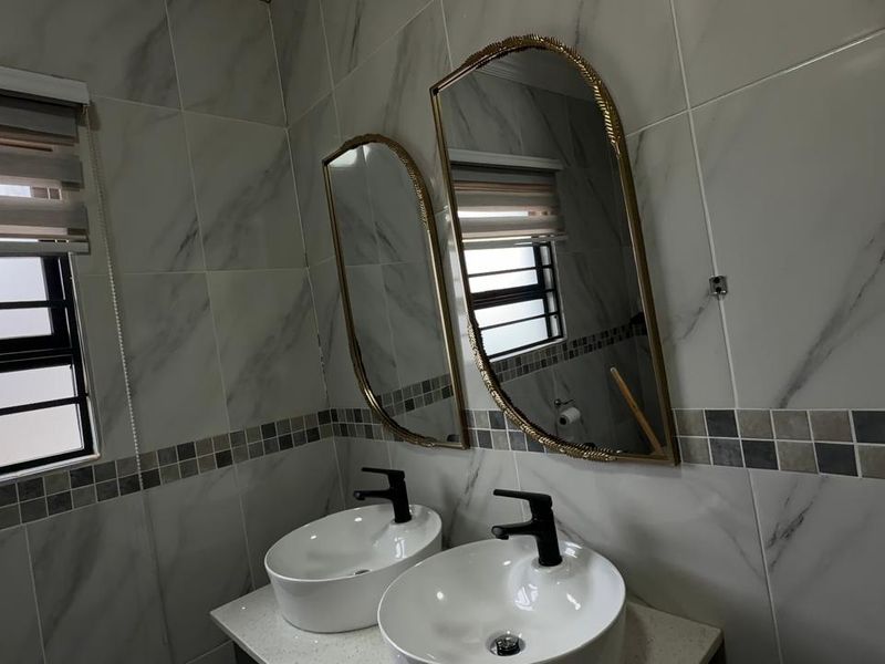 Modern bathroom featuring a double vanity with vessel sinks, black fixtures, and elegant marble-look wall tiling with a decorative mosaic border.