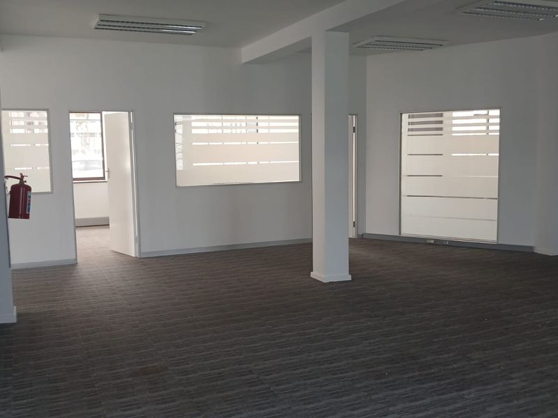 A spacious, empty office area featuring neutral walls, carpeted flooring, recessed lighting, and frosted glass partitions for a professional, modern workspace.
