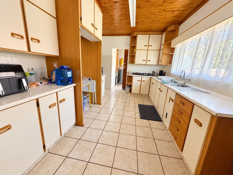 A functional kitchen featuring extensive built-in cabinetry, tiled flooring, a timber ceiling, and a double sink with ample counter space.