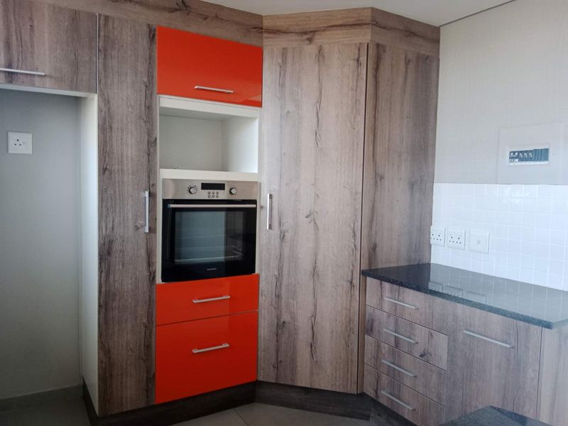 Modern kitchen featuring wood-grain cabinetry with vibrant orange accents, a built-in oven, granite countertops, and a clean tiled backsplash.