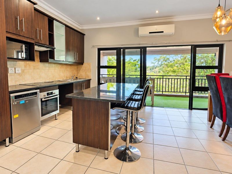 Modern open-plan kitchen and dining area featuring dark wood cabinetry, granite countertops, a central island, and direct access to a balcony through sliding doors.