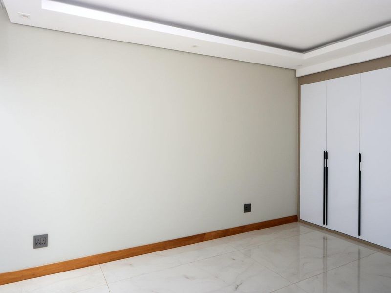 A bright, empty bedroom featuring modern tiled flooring, recessed ceiling lighting, and a sleek built-in wardrobe with contemporary hardware.