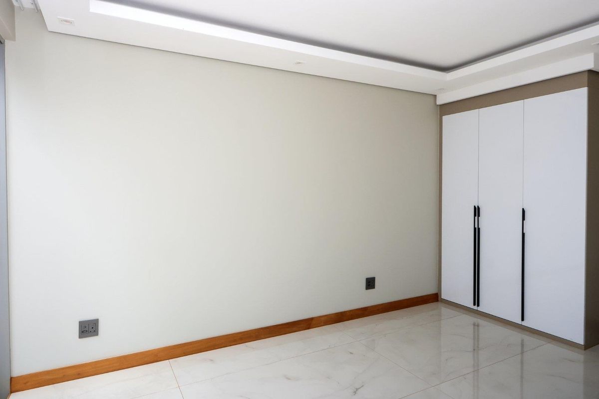 A bright, empty bedroom featuring modern tiled flooring, recessed ceiling lighting, and a sleek built-in wardrobe with contemporary hardware.