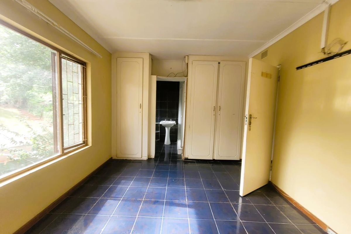 A bedroom featuring dark tiled flooring, built-in cupboards, and an en-suite bathroom area with a pedestal basin.