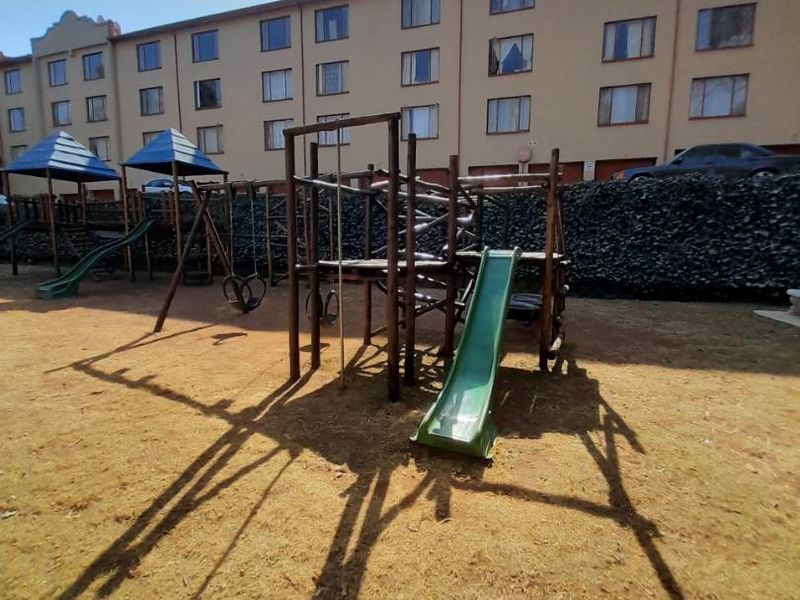 Communal outdoor area featuring a playground set and stone retaining wall, situated at the rear of the apartment complex.