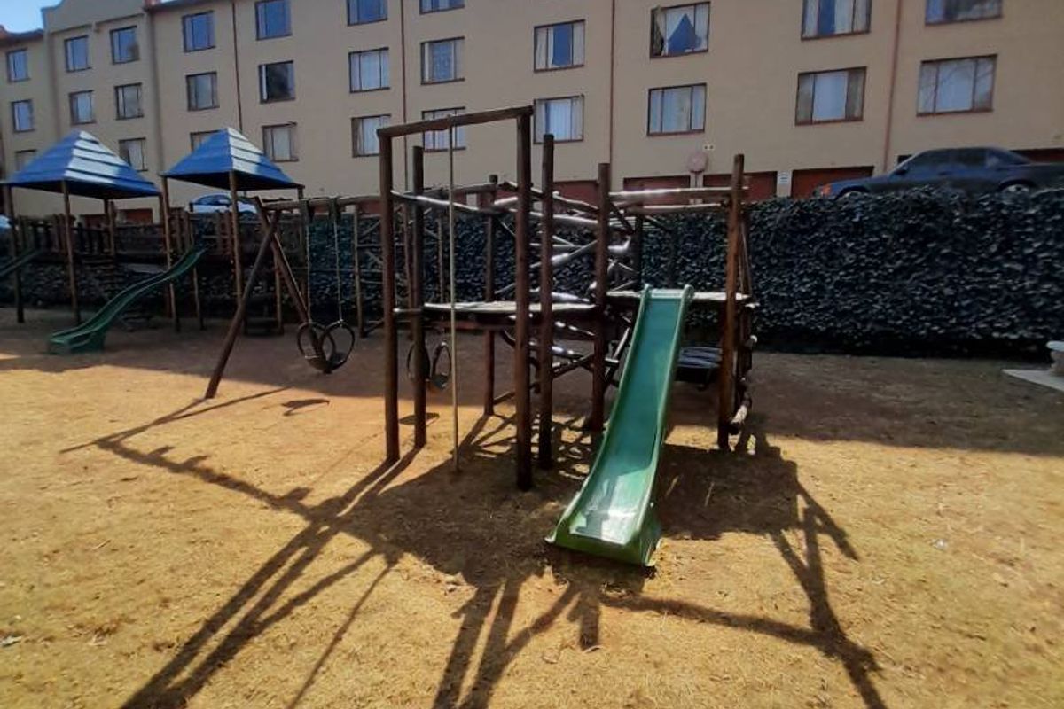 Communal outdoor area featuring a playground set and stone retaining wall, situated at the rear of the apartment complex.