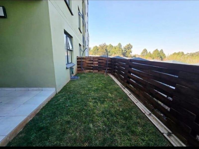 A private garden area featuring a small tiled patio, a well-maintained lawn, and timber slat perimeter fencing.