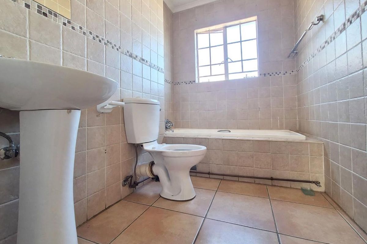 A dated bathroom featuring a pedestal basin, toilet, and built-in bathtub with full-height wall tiling and tiled flooring.