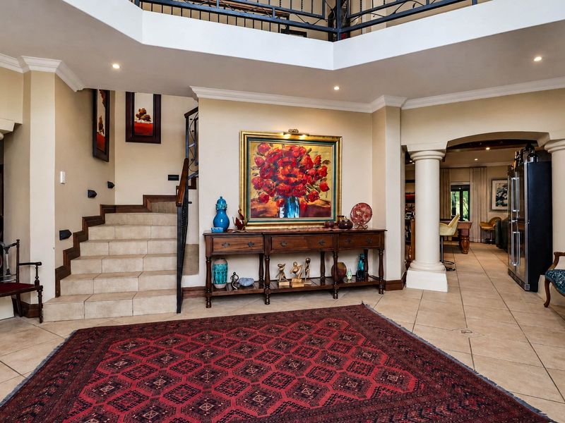 Spacious double-volume entrance hall featuring tiled flooring, a grand staircase with wrought iron balustrades, and elegant architectural columns leading to the living areas.