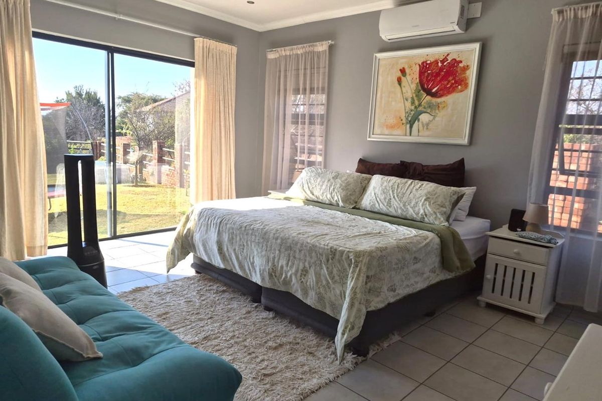 Spacious bedroom featuring tiled flooring, a split-system air conditioner, and large sliding glass doors providing direct access to the rear garden.