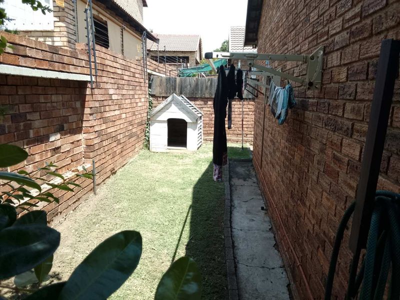 A narrow rear garden area featuring a brick boundary wall with electric fencing, a concrete pathway, and a wall-mounted clothesline.