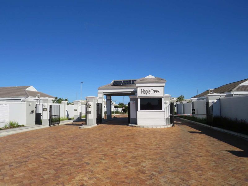 The secure entrance gate and guard house of MapleCreek estate, featuring paved driveway access and solar panel installation.