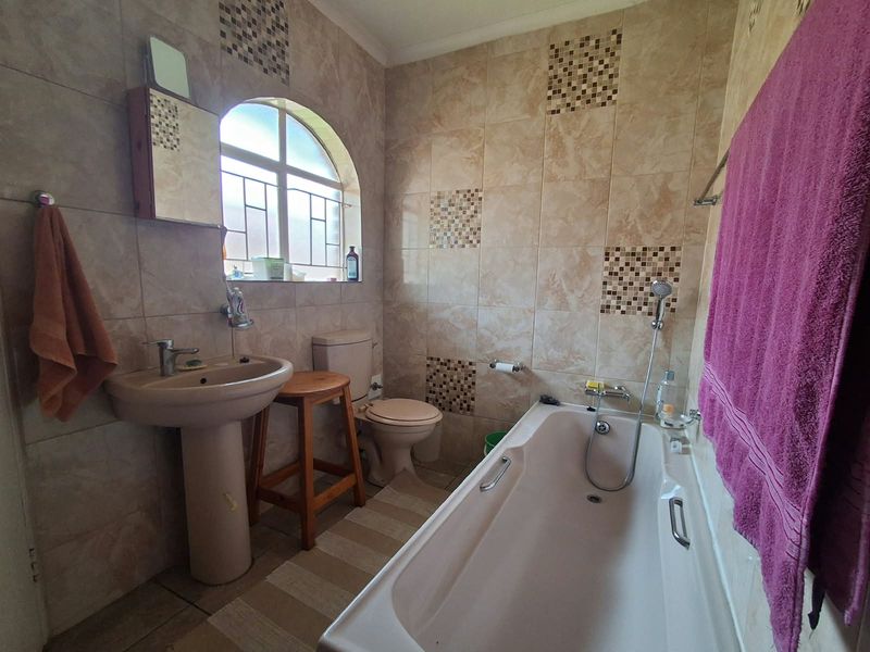 A functional bathroom featuring a pedestal basin, toilet, and bathtub with a handheld shower mixer, finished with neutral wall and floor tiling.