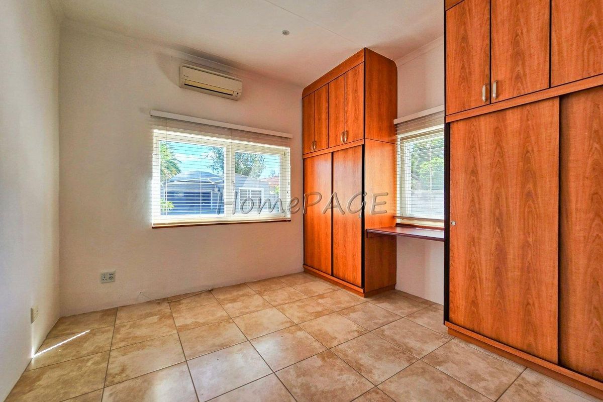 A bedroom featuring built-in wooden cabinetry with an integrated desk, tiled flooring, and a wall-mounted air conditioning unit.