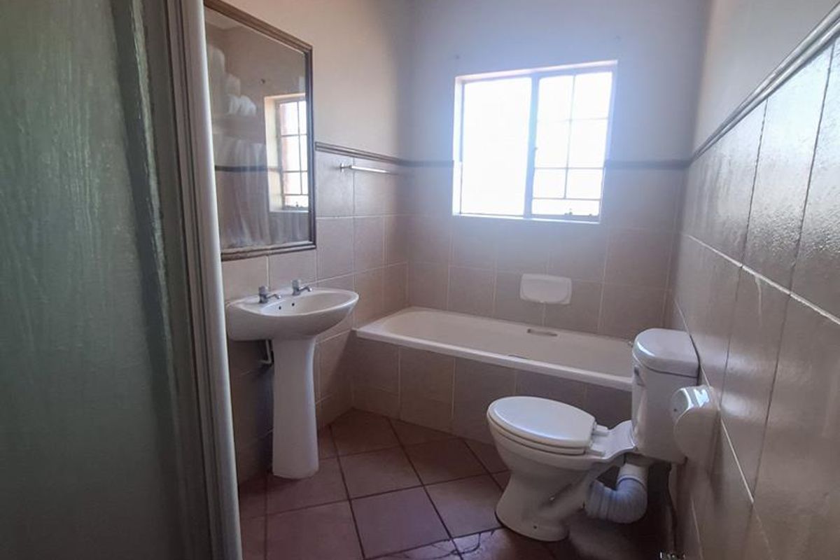 A dated bathroom featuring a pedestal basin, bathtub, and toilet with tiled walls and flooring, requiring modernization.