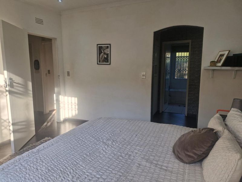 A bedroom featuring laminate flooring, recessed lighting, and an arched doorway leading to an adjoining bathroom area with security gate.
