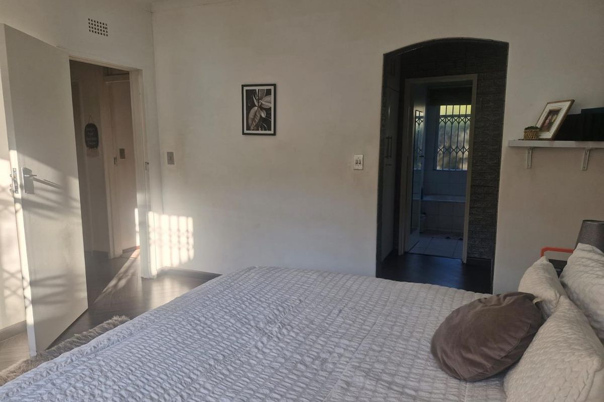 A bedroom featuring laminate flooring, recessed lighting, and an arched doorway leading to an adjoining bathroom area with security gate.