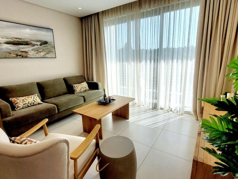 A bright and modern living room featuring large format floor tiles, recessed lighting, and expansive floor-to-ceiling glass doors leading to an outdoor area.