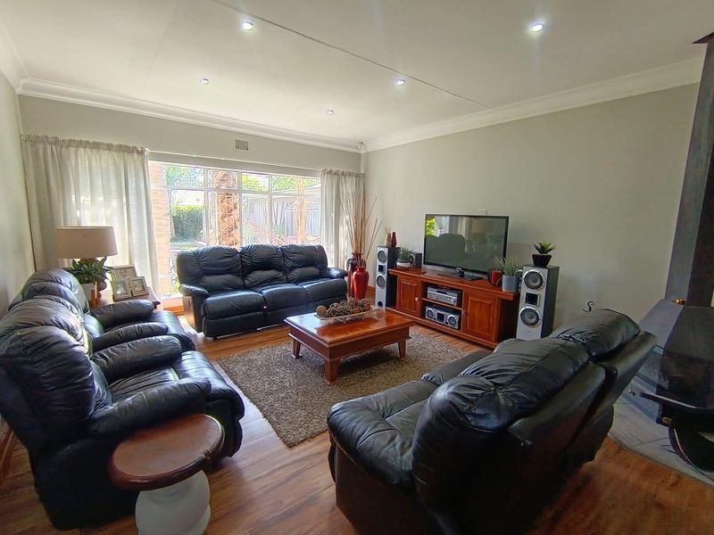 Spacious living room featuring laminate flooring, recessed downlighting, and a fireplace, with large windows providing natural light and garden views.