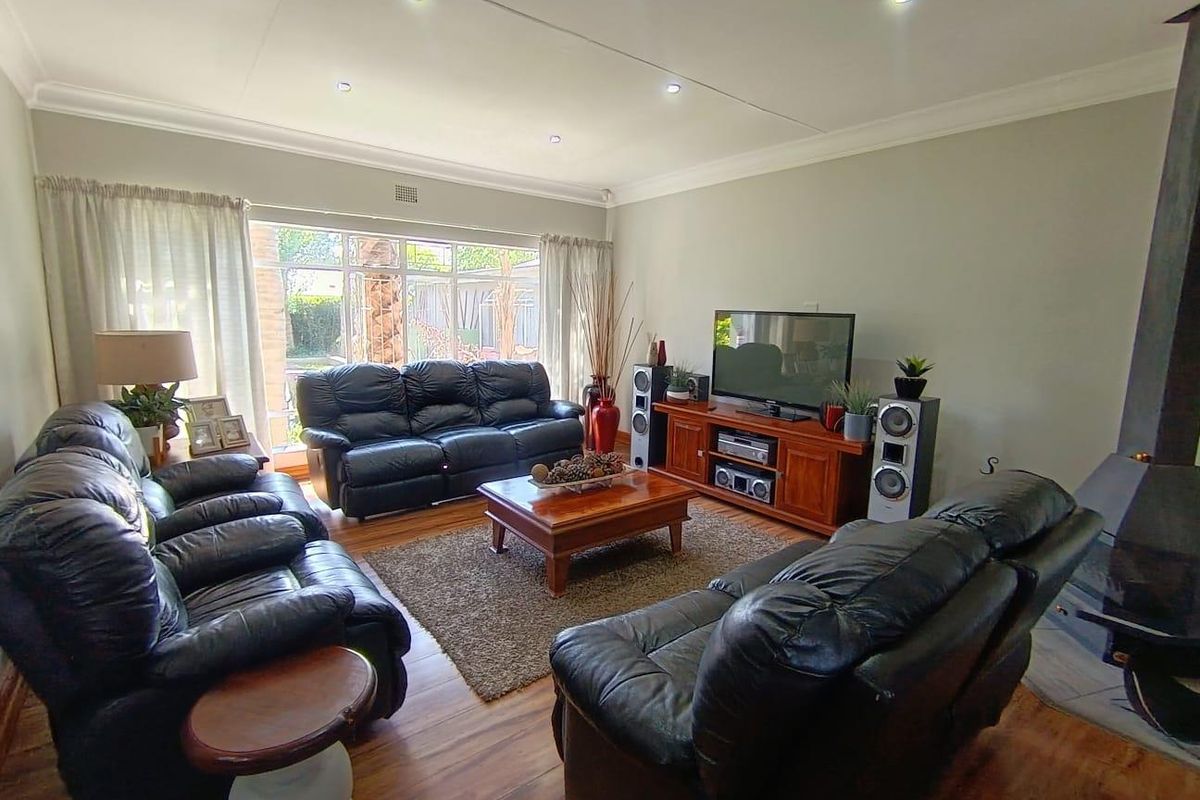 Spacious living room featuring laminate flooring, recessed downlighting, and a fireplace, with large windows providing natural light and garden views.