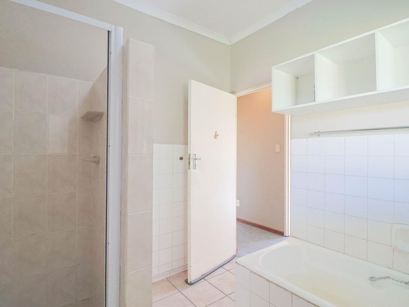 A functional bathroom featuring a shower enclosure, built-in bathtub, and tiled finishes, offering a blank canvas for modern updates.