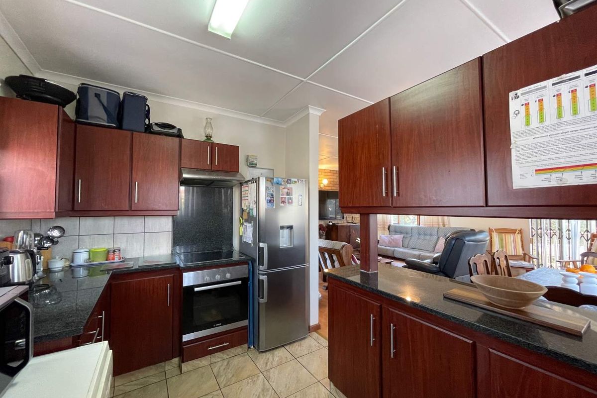 Functional kitchen featuring dark wood cabinetry, granite countertops, tiled flooring, and a built-in oven with extractor fan, opening into the adjacent living area.