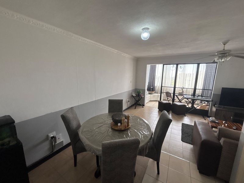 Open-plan living and dining area featuring tiled flooring, decorative ceiling cornices, and large sliding glass doors leading to a balcony.