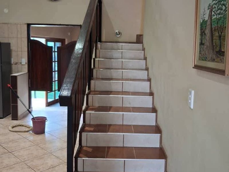 A staircase featuring tiled steps and a wooden handrail, leading from a tiled hallway area.