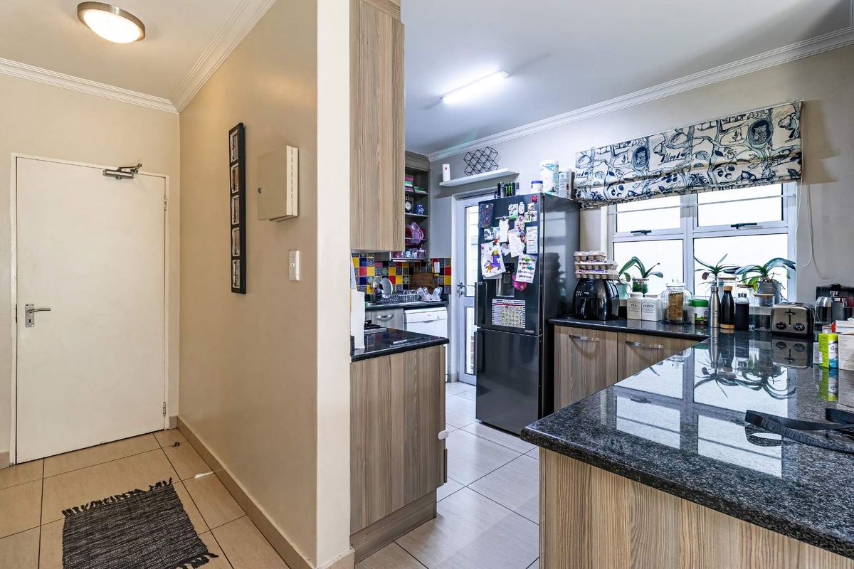 A functional kitchen featuring granite countertops, wood-look cabinetry, and a mosaic tile backsplash, with direct access to an exterior door.