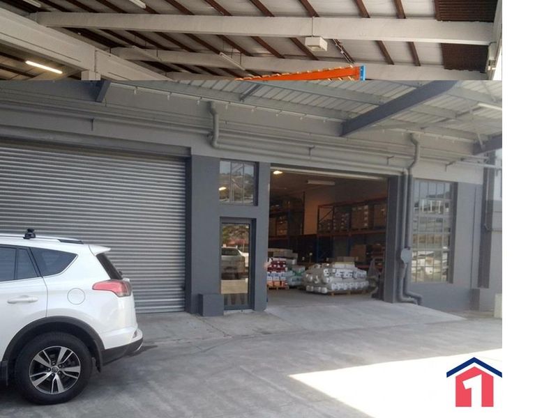 Industrial warehouse exterior featuring a roller shutter door, steel frame construction, and exposed roof trusses, providing functional access for commercial operations.